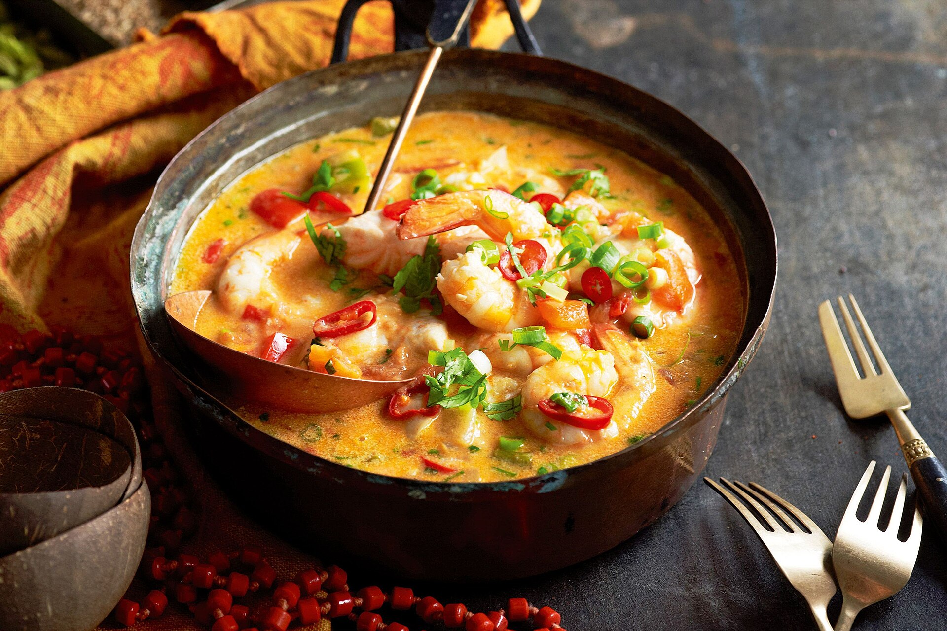 A pot of moqueca with seafood and colorful vegetables on a table.